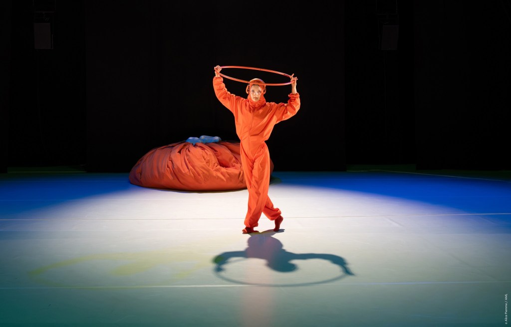 circus artist Laura Savolainen on stage with an orange overall and an orange hula hoop